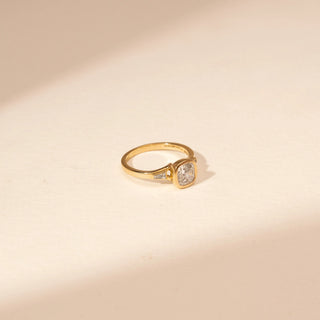 Side view of a 14KT Yellow Gold ring with a bezel-set cushion centre diamond and baguette side diamonds.