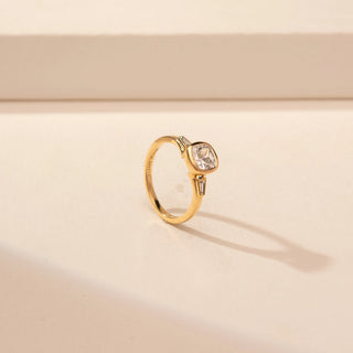 Angled view of a 14KT Yellow Gold ring with a bezel-set cushion centre diamond and baguette side diamonds.