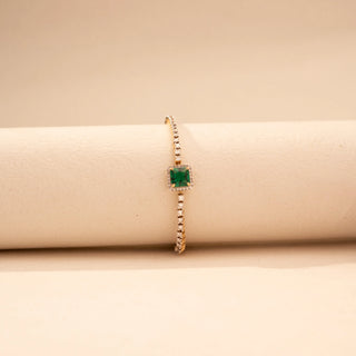 Front view of a  Round lab-grown diamond tennis bracelet in 14 KT yellow gold, featuring a square emerald centre stone framed by a diamond halo with a continuous row of round brilliant diamonds in an elegant design.