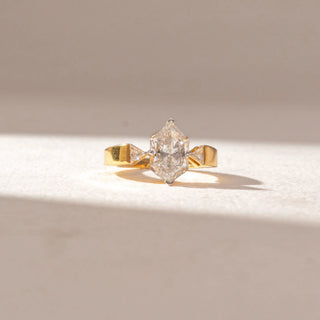 Front view of elongated hexagon diamond ring in yellow gold, flanked by tapered side stones, set on a soft neutral surface, highlighting bold geometry and crisp, radiant brilliance.
