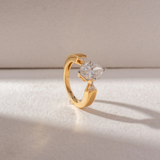 Angled view of elongated hexagon diamond ring in yellow gold with tapered side stones, set on a soft neutral background, highlighting bold edges and elevated, radiant sparkle.
