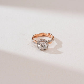 Front view of the Intertwined Rose Gold Diamond Ring in 14KT rose gold, featuring a round brilliant center diamond with a cushion-shaped halo and a twisted shank with pavé diamonds on a neutral background.
