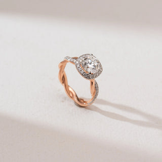 Angled view of the Intertwined Rose Gold Diamond Ring in 14KT rose gold, showcasing a round brilliant center diamond with a cushion halo and a twisted dual-tone shank accented with pavé diamonds.