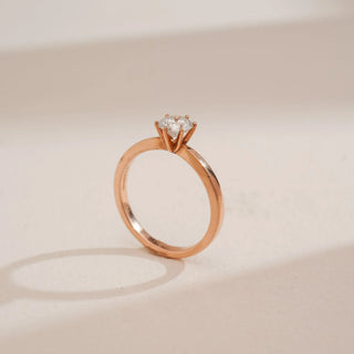 Side view of Reia’s 14 KT Rose Gold Classic Grace Round Diamond Ring. Captured against a cream backdrop, the layout highlights the delicate six-prong setting and polished band.