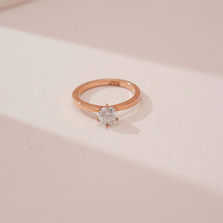 Angled top view of Reia’s 14 KT Rose Gold Classic Grace Round Diamond Ring. Captured against a cream backdrop, the layout highlights the timeless beauty of the single, radiant stone.