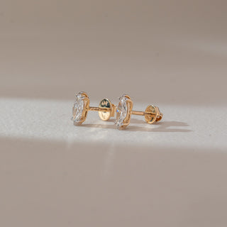 Side view of marquise diamond stud earrings in white gold, featuring elongated lab-grown diamonds in a prong setting. Captured against a soft beige background with gentle shadows.