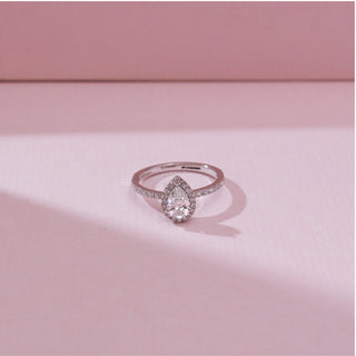 Angled front view of the Pear Halo Radiant Diamond Ring in 14KT white gold, showcasing a pear-shaped center diamond surrounded by a sparkling halo and pavé-set diamond band on a soft pink background.