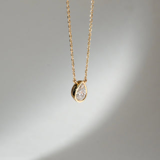 Angled view of Pear Bezel Diamond Pendant Necklace in 14KT Yellow Gold, featuring a pear-shaped lab grown diamond in a sleek bezel setting. Set on a neutral backdrop, the design highlights depth, polish and refined brilliance.
