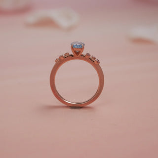 Side view of Reia Ocean Mist Cushion Diamond Ring on a blush-peach background, highlighting the raised azure cushion-cut centre diamond set on a 14KT white gold band adorned with EF VVS accent stones.