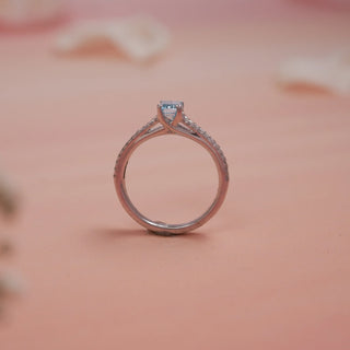 Side view of Reia Azure Emerald-Cut Diamond Ring on a blush-peach background, showing the elegant cross-over band in 14KT white gold with pave-set EF VVS diamonds and a striking blue centre stone.