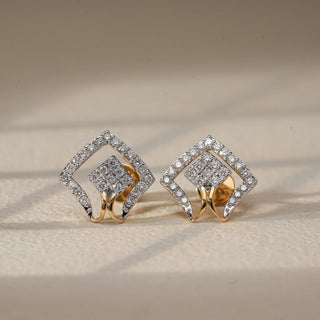 Captured in a direct front-facing view on a softly lit beige surface, a pair of 14 KT yellow gold diamond stud earrings showcases a bold, sculptural design. Each earring features dual diamond-shaped frames—one nested inside the other—adorned with EF-color, VVS-clarity round diamonds totaling 0.580 carats.