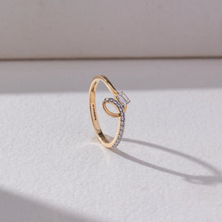 Side view of Baguette Solitaire Diamond Ring in 14KT Yellow Gold, featuring an emerald-cut lab grown diamond with a pavé crossover band. Set on a beige backdrop, the design highlights structure and refined elegance.
