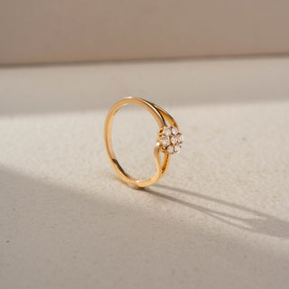 Angled view of a floral diamond ring in 14 KT Yellow Gold, featuring a flower-shaped cluster of round lab-grown diamonds nestled within a flowing open-band design, displayed against a beige backdrop.