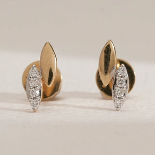 Close-up of petite leaf-shaped stud earrings in 14KT Yellow Gold, featuring one polished gold leaf and one diamond-studded leaf with round-cut diamonds, secured with Bombay screw backs.