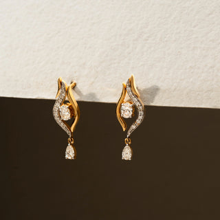 Side view of diamond drop earrings in 14 KT Yellow Gold, featuring flowing pavé-set curves, floating round diamonds, and pear-shaped dangling accents against a neutral backdrop.