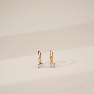 Front angled view of yellow gold solitaire diamond hoop earrings featuring round lab-grown diamonds set at the base of slim polished hoops against a soft neutral studio background.