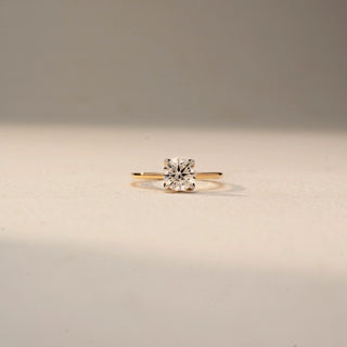 Front view of a classic solitaire diamond ring featuring a round brilliant-cut center stone set on a sleek yellow gold band, displayed against a soft neutral background.