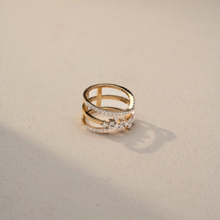 Top top view of a diamond wrap ring in 14 KT Yellow Gold, featuring pavé-set diamond bands and floral-inspired diamond clusters in an elegant open crossover design, displayed against a beige backdrop.