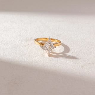 Top view of step-cut kite-shaped diamond ring in yellow gold with a slim band, set on a soft neutral surface, highlighting geometric lines and crisp, reflective brilliance.
