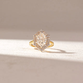 Front view of Geometric Diamond Statement Ring in 14KT Yellow Gold, featuring a large center diamond framed by baguette and round accents. Set on a soft beige surface, the design reflects bold brilliance and symmetry.
