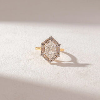 Top view of Geometric Diamond Statement Ring in 14KT Yellow Gold, featuring a central diamond framed by baguette and round accents. Set on a soft beige surface, the design reflects symmetry and brilliance.
