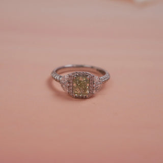 Side view of Reia Verdant Halo Radiant Diamond Ring on a blush-peach background, highlighting the elevated green centre stone and intricate diamond halo design on a pave-set 14KT white gold band.