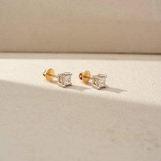 Side view of princess-cut diamond stud earrings in yellow gold, featuring square diamonds in elevated basket settings. Displayed on a beige backdrop, the profile showcases intricate craftsmanship.