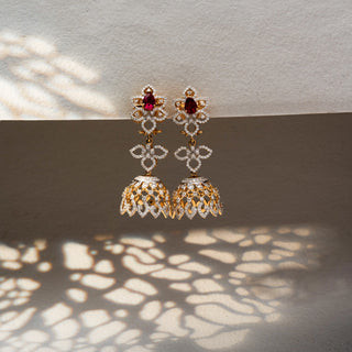Front view of floral diamond jhumka earrings in 14 KT Yellow Gold, featuring ruby-toned pear stones, open floral motifs, and lattice dome drops against a neutral backdrop.