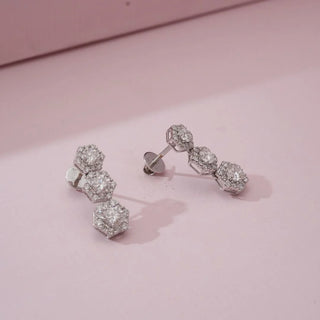 Top-angled view of hexagon triple cluster diamond earrings with round lab-grown diamonds in stacked geometric settings, placed on a soft pink background under diffused studio lighting.
