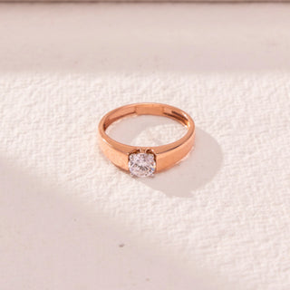 Top view of a 14KT rose gold ring featuring a round-cut diamond, set against a beige background.