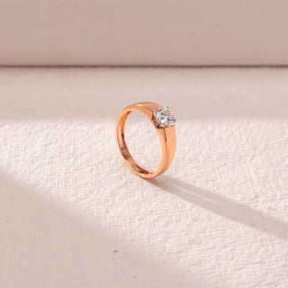 Angled view of a 14KT rose gold ring featuring a round-cut diamond, set against a beige background.