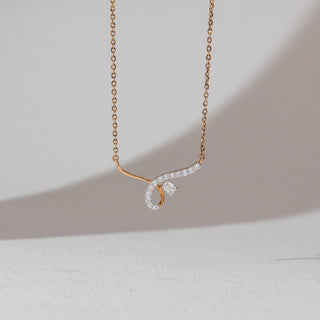 Angled view of diamond pendant necklace in yellow gold, featuring a curved lab-grown diamond-studded design with a central baguette diamond. Captured against a soft neutral background.