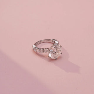 Side view of a round solitaire ring in White Gold, featuring a round-cut lab-grown diamond in a six-prong setting with diamond-accented shoulders, displayed against a soft pink backdrop.