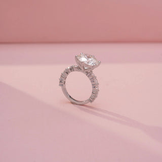 Angled view of a round solitaire ring in White Gold, featuring a round-cut lab-grown diamond in a six-prong setting with diamond-accented shoulders, displayed against a soft pink backdrop.