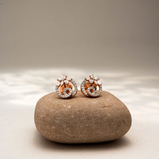 Front view of floral diamond stud earrings in 14 KT Yellow Gold, featuring pavé-set swirling motifs with marquise and round diamond accents, displayed on a textured stone surface.
