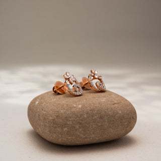 Side view of floral diamond stud earrings in 14 KT Yellow Gold, featuring pavé-set swirling motifs with marquise and round diamond accents, displayed on a textured stone surface.