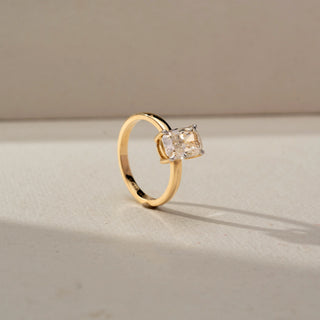 Angled view of a yellow gold solitaire ring featuring a cushion-cut diamond in a four-prong setting, showcasing its elevated profile, clean band, and radiant sparkle against a neutral backdrop.