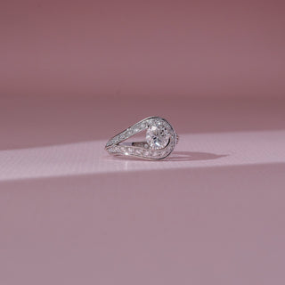 Front view of solitaire diamond ring in white gold, featuring a round lab-grown diamond set within a curved teardrop frame lined with round diamonds. Set against a soft pink backdrop, it reflects fluid elegance.