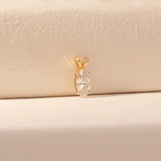 Side view of a 14KT yellow gold pendant featuring a marquise-cut diamond, set against a beige background.