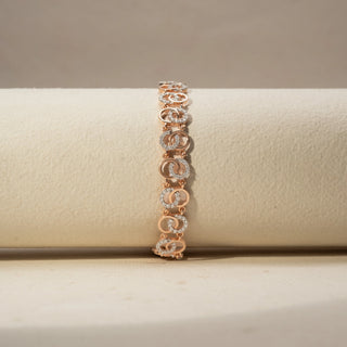 Front view of a diamond bracelet in 14 KT Rose Gold, featuring interlocking oval motifs accented with pavé-set diamonds in a graceful linked design, displayed against a soft beige backdrop.
