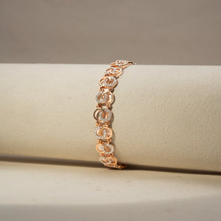 Close Up view of a diamond bracelet in 14 KT Rose Gold, featuring interlocking oval motifs accented with pavé-set diamonds in a graceful linked design, displayed against a soft beige backdrop.

