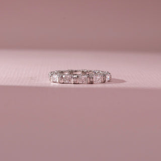 Front view of eternity band in white gold with square and rectangular diamonds in prong settings, set on a soft pink background, highlighting varied cuts and continuous, radiant sparkle.
