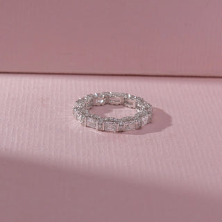 Top view of eternity band in white gold with square and rectangular diamonds in prong settings, set on a soft pink textured surface, highlighting varied cuts and continuous, radiant sparkle.
