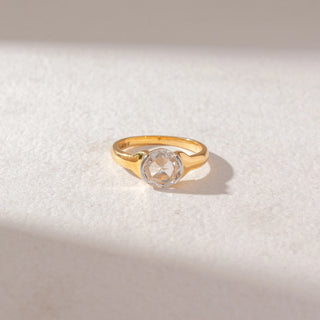 Top view of round diamond solitaire ring in yellow gold with a smooth tapered band, set on a soft neutral surface, highlighting classic design and soft, radiant sparkle.
