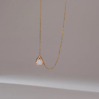 Close-up view of solitaire diamond pendant necklace in yellow gold, featuring a round lab-grown diamond set within a smooth teardrop frame on a delicate chain. Set against a soft neutral backdrop, it reflects minimal elegance.