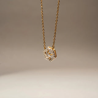 Close Up view of a geometric diamond pendant necklace in 14 KT Yellow Gold, featuring a hexagonal pavé-set frame with a floating round center diamond suspended on a delicate gold chain.

