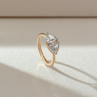Side view of toi et moi diamond ring in yellow gold, featuring two pear-shaped lab-grown diamonds set opposite each other. Placed on a textured beige surface, the design casts a soft elongated shadow.

