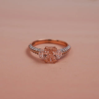 Front view of Reia Rose Glow Emerald Diamond Ring on a blush-peach background, displaying the radiant blush emerald diamond centre stone with accent diamonds in a rose gold setting.