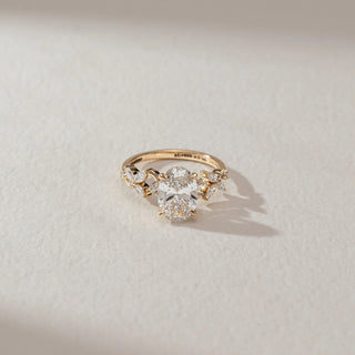 Top view of solitaire diamond ring in yellow gold, featuring a large oval lab-grown diamond at the centre with marquise-shaped diamond accents on the band. Set on a soft neutral surface, it reflects refined brilliance.