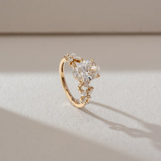 Side angled view of solitaire diamond ring in yellow gold, featuring a large oval lab-grown diamond with marquise-shaped diamond accents along the band. Set on a soft neutral backdrop, it highlights brilliance and detail.